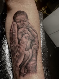 a black and grey tattoo of a baby in a hand