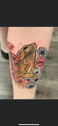a tattoo of a frog with flowers on her thigh
